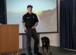 Dallas Seavy with a sled dog speaking at APU