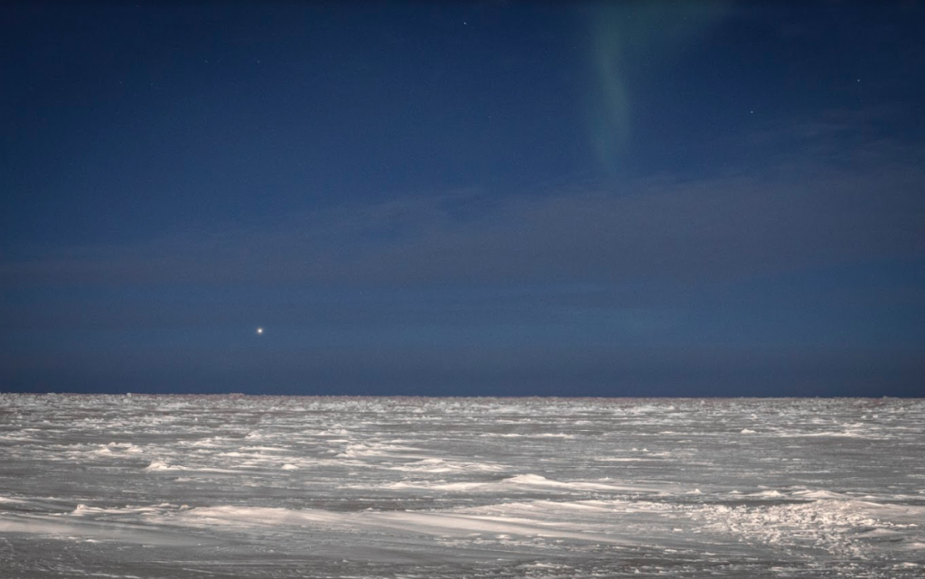 The Arctic Ocean at night with a faint hint of Northern Lights dancing in the dark untouched sky.