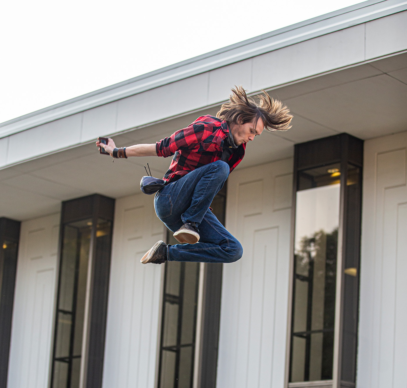 A person mid-air performing a blanket toss in front of a modern building with vertical windows, watched by a crowd below.