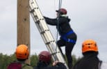 A student climbs a ropes course ladder