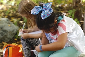Two elementary students writing in notebooks outside