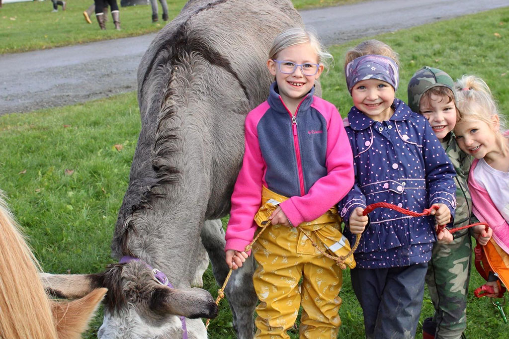 four kids holding a rope attached to a donkey, smiling