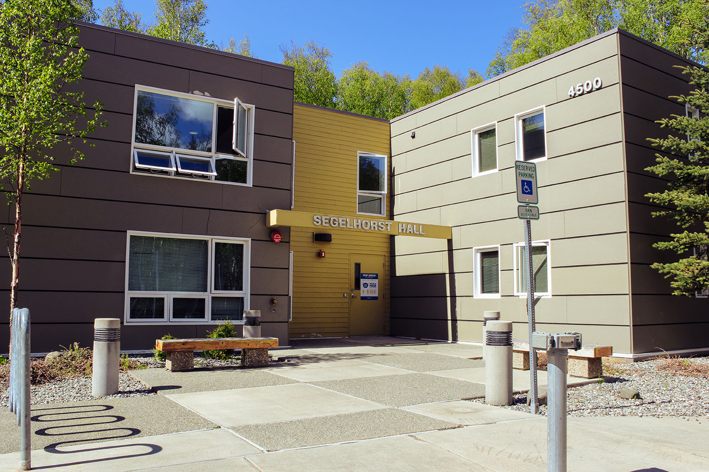 Modern building labeled Segehorst Hall with a yellow entrance, surrounded by trees and a clear blue sky.