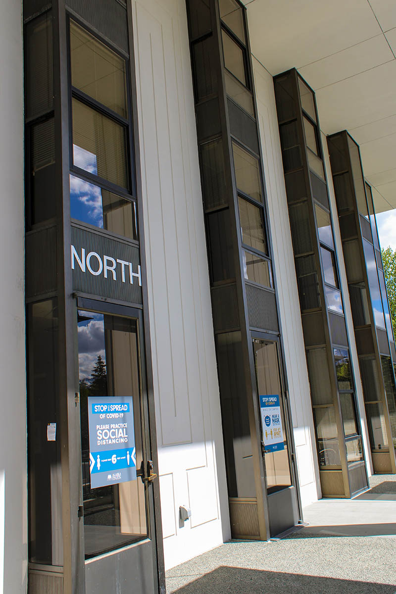 The entrance to a building labeled "NORTH" with a sign about practicing social distancing to prevent the spread of COVID-19.