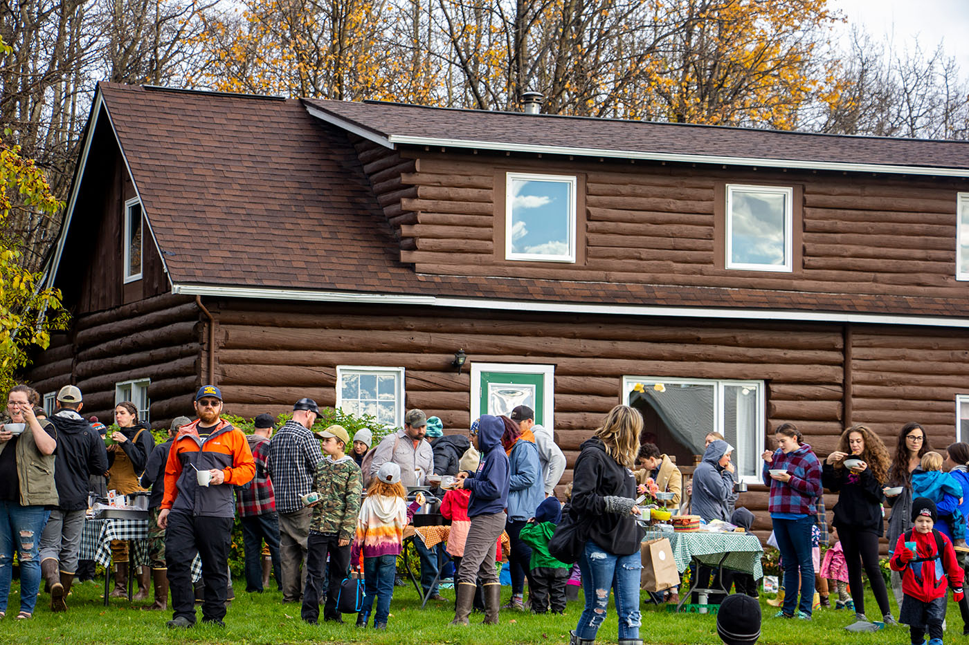 A log cabin with a group of people gathered outside, enjoying food and conversation.