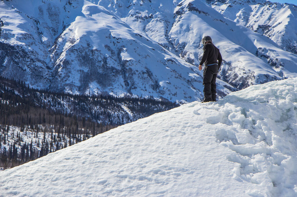 A person stands on a snowy ridge overlooking a vast mountain range.