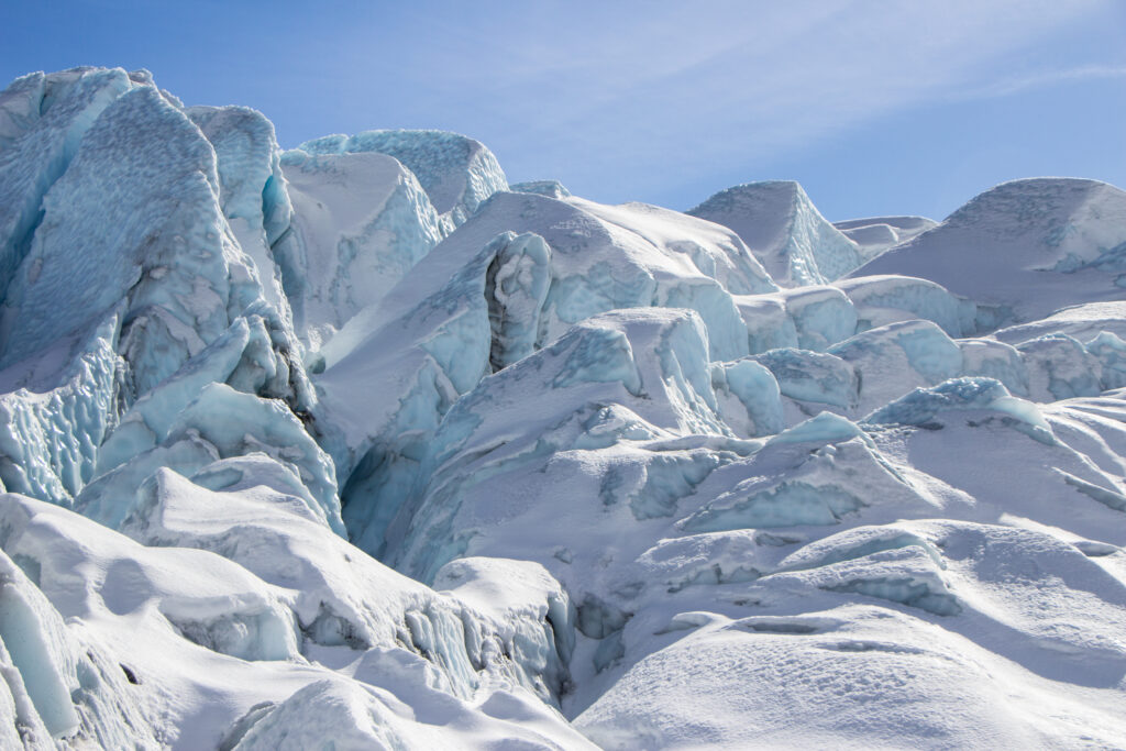 A close-up view of a glacier with jagged ice formations under a clear blue sky.