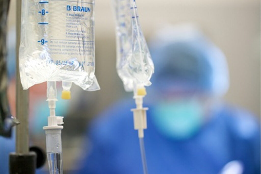 IV drip bags with tubes, set against a blurred background of a medical professional in blue scrubs.