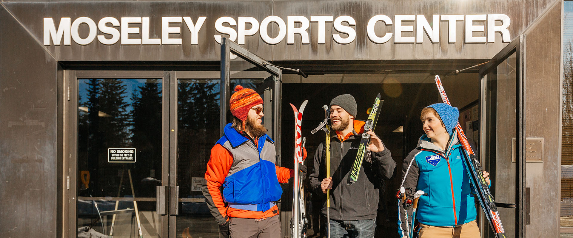 students coming out of the Moseley Sports Center, talking and holding skis
