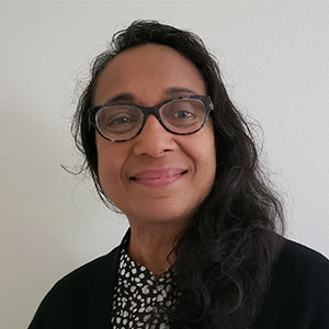 A person with glasses and long dark hair smiling indoors.